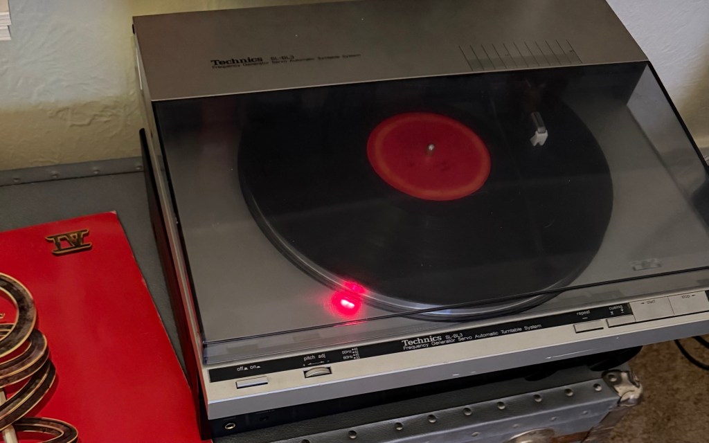 A restored 1983 Technics turntable playing a vinyl record beside an old Styx album on a quiet Sunday afternoon.